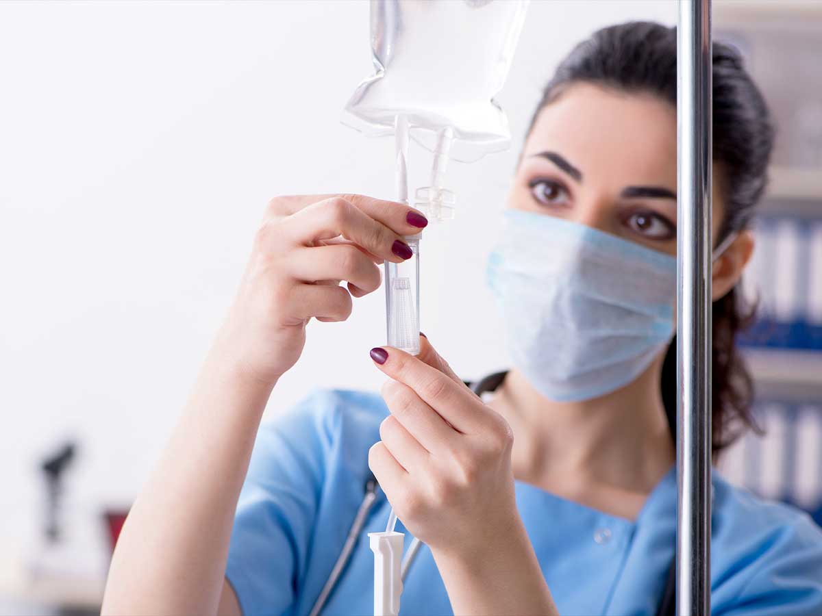 Medizinisches Personal (Frau) stellt eine Infusion in einem Krankenhaus ein. Infusionen werden aus Weich-PVC hergestellt, das in der Regel mit BUSS-Compoundierern produziert wird.